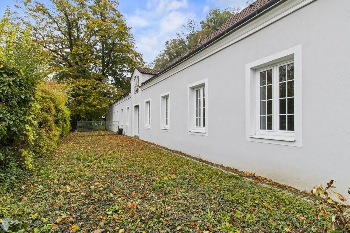 Ansicht der langen weißen Fassade eines historischen Gebäudes mit vielen Fenstern und einem gepflegten Rasenbereich.
