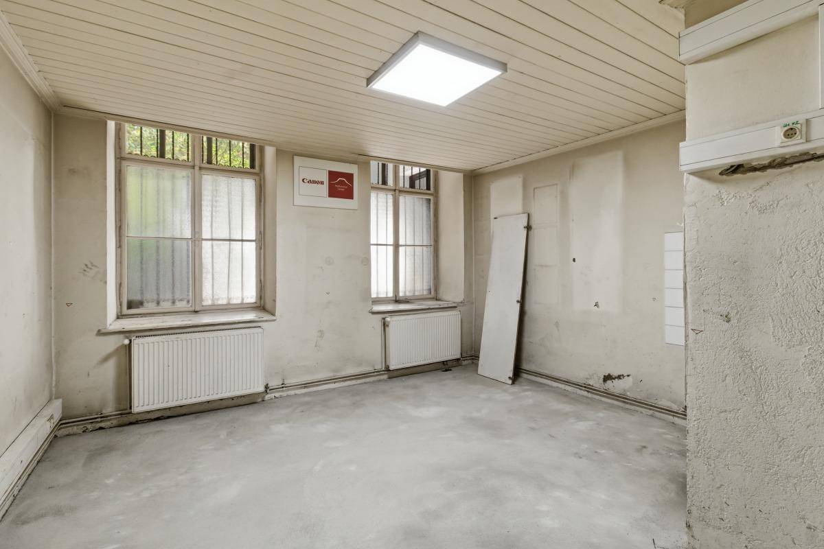 Raum mit zwei Fenstern, Heizkörpern und einer Holzdecke, der als Büro oder Lagerraum genutzt werden könnte.