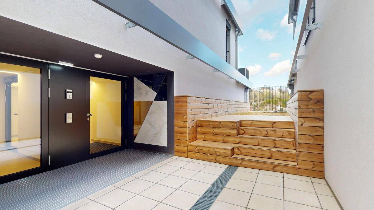 Moderner Eingangsbereich des Gebäudes mit Holzverkleidung und gepflastertem Vorplatz.