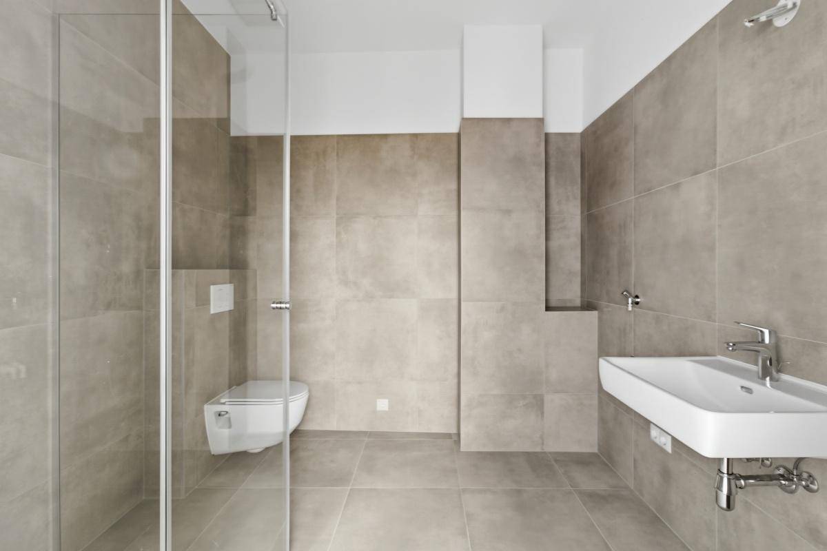 Modernes Badezimmer mit beigefarbenen Fliesen, wandhängendem WC und einer geräumigen Glasdusche.