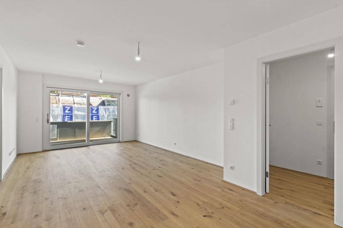 Geräumiger, heller Wohnraum mit Holzboden und direktem Zugang zum Balkon.