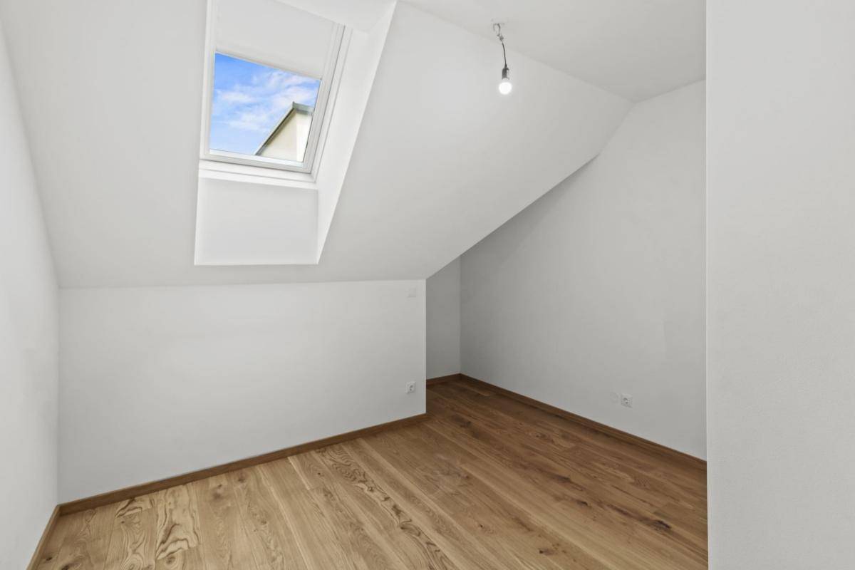 Helles Schlafzimmer mit Holzboden, Dachschräge und einem Dachfenster für natürliches Licht.