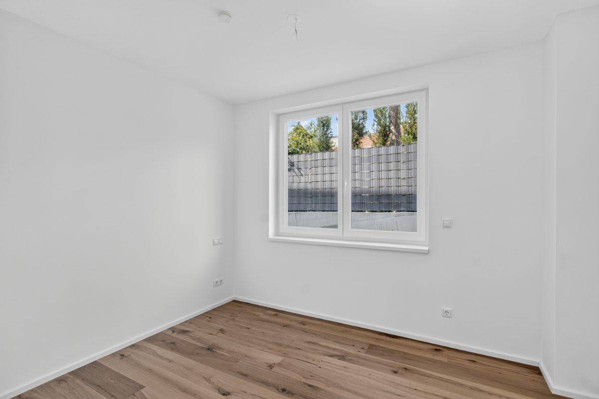 Helles Schlafzimmer mit Holzboden und Fenster, das einen Blick ins Grüne bietet.