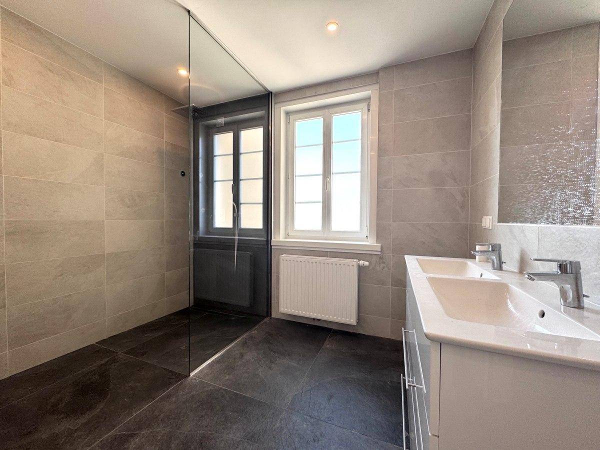 Elegantes Badezimmer mit begehbarer Dusche, Doppelwaschbecken und modernen grauen Fliesen.
