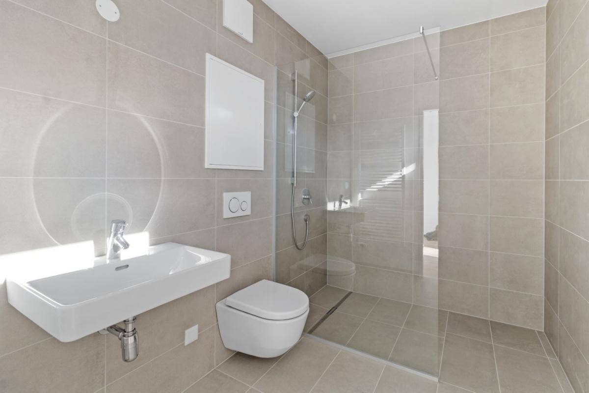 Modernes Badezimmer mit hellgrauen Fliesen, wandhängendem WC und ebenerdiger Dusche.