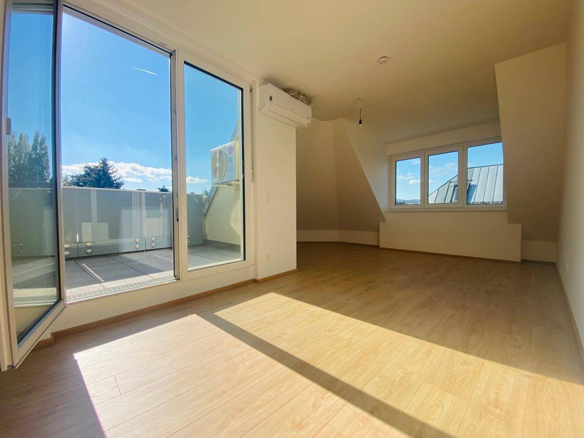 Helles Wohnzimmer mit Holzboden, Dachschrägen und Zugang zu einer sonnigen Terrasse.