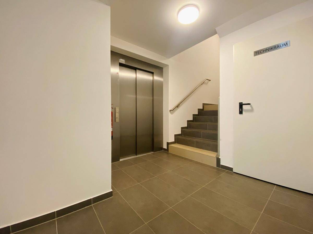 Eingangsbereich des Gebäudes mit Aufzug, Treppenhaus und Fliesenboden.