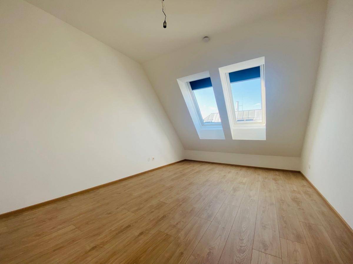Helles Zimmer mit Laminatboden, Dachschrägen und Dachfenstern mit Blick nach draußen.