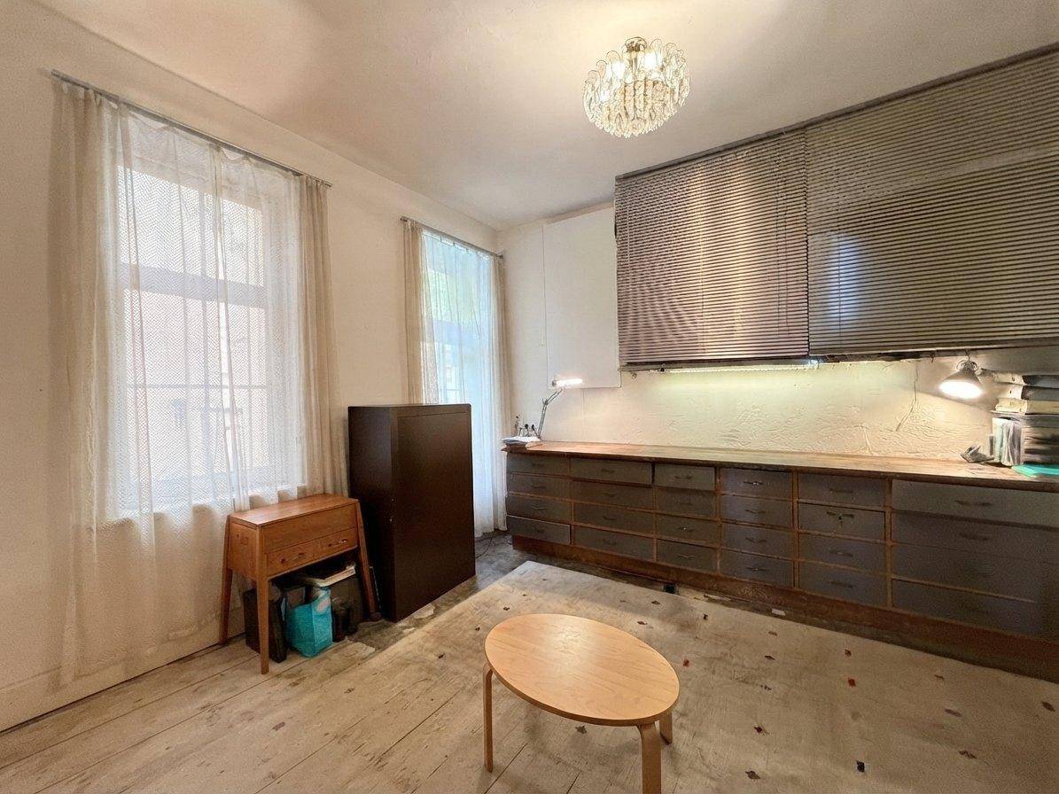 Büroraum mit zwei Fenstern, Holzboden und einem großen Schreibtisch mit vielen Schubladen und Jalousien.