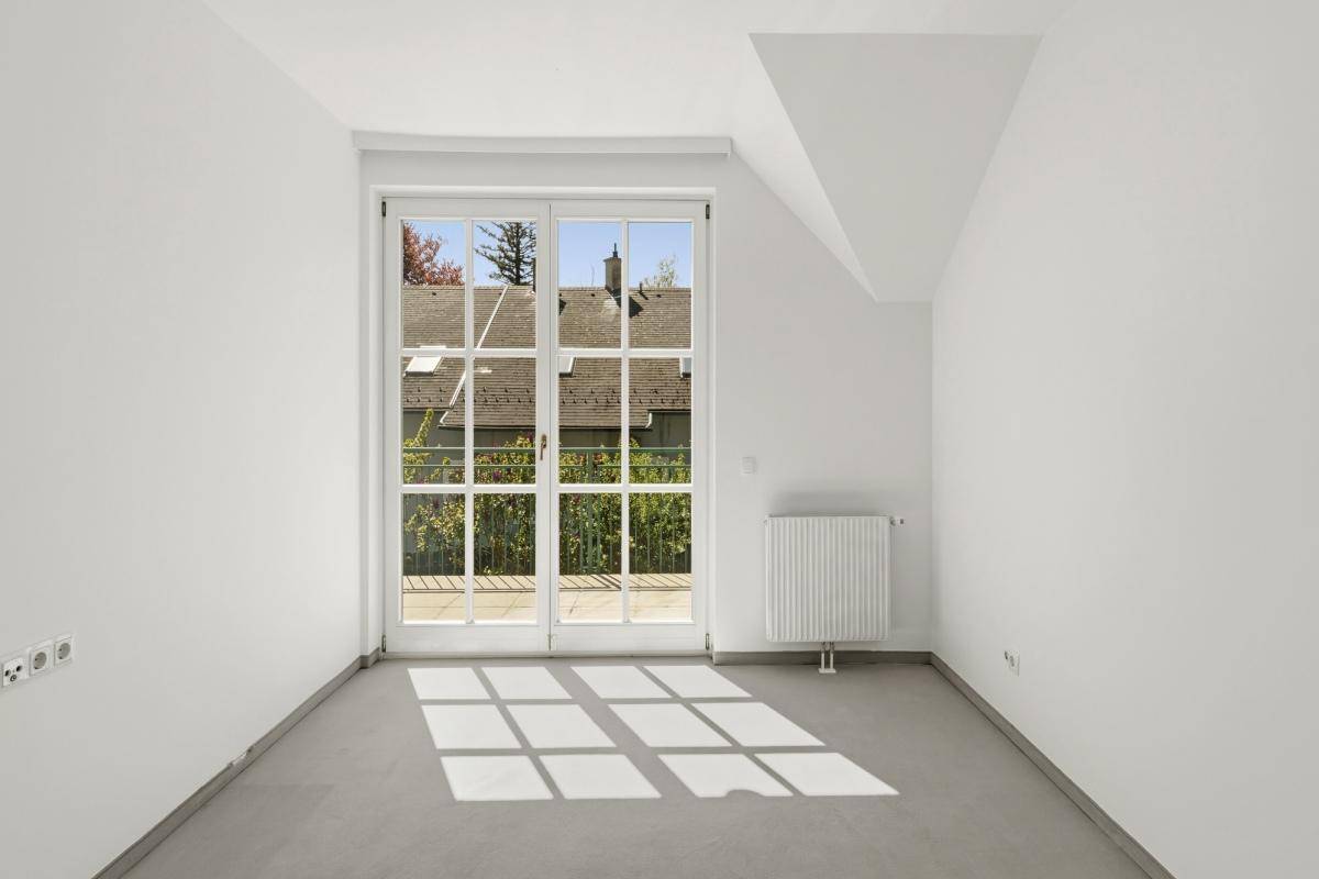 Geräumiges Zimmer mit Teppichboden, schrägen Wänden und Zugang zu einem Balkon.