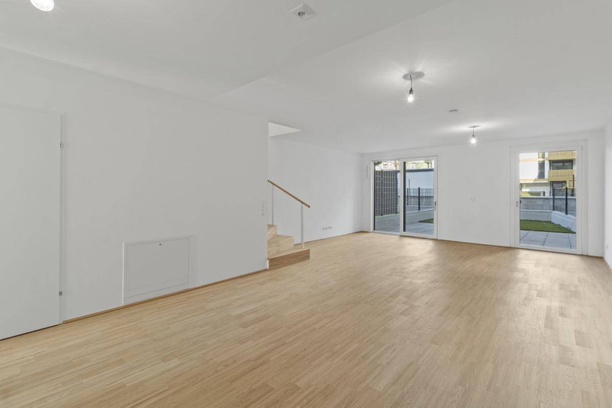 Geräumiges, leeres Wohnzimmer mit Holzboden und Zugang zu einer Terrasse oder Garten.