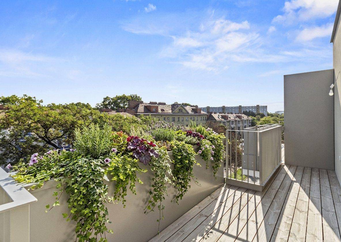 Geräumiger Balkon mit Holzbelag und üppigen Pflanzen, bietet einen grünen Ausblick.