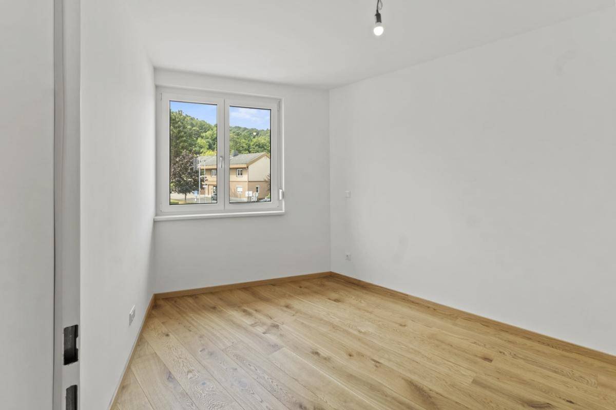 Geräumiges Schlafzimmer mit Parkettboden und Fenster mit weitem Blick ins Grüne.