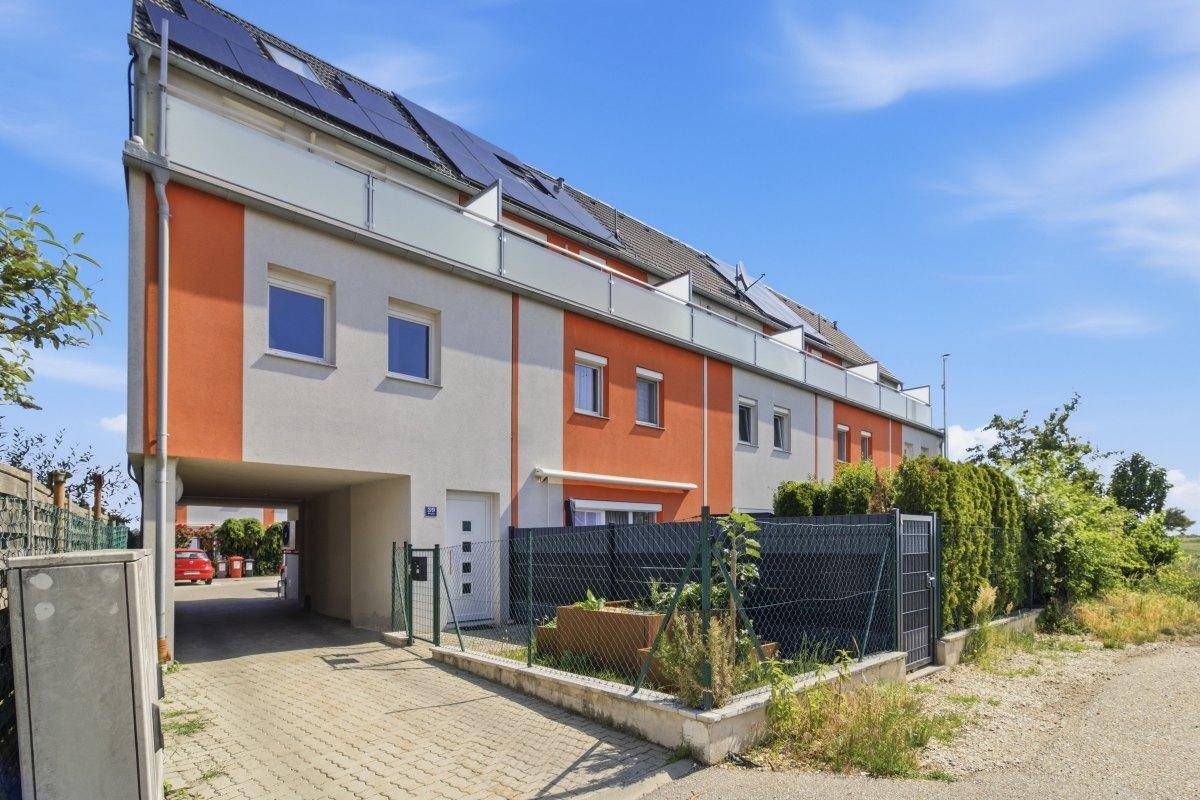 Moderne Reihenhäuser mit orangefarbener Fassade, Carport und Solaranlagen auf dem Dach.