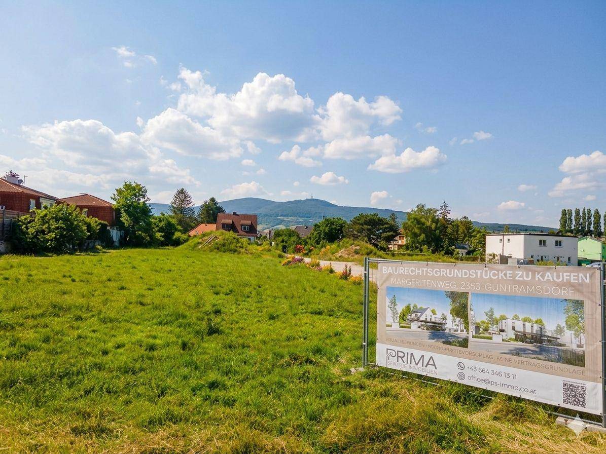 Großes grünes Baugrundstück mit Immobilienwerbetafel und Blick auf die umliegende Landschaft.