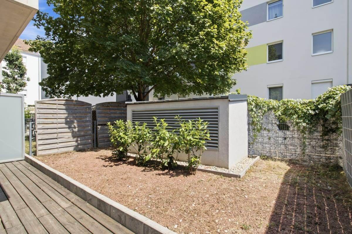 Außenbereich mit Holzterrasse und vorbereiteter Gartenfläche, umgeben von einer Gabionenwand.