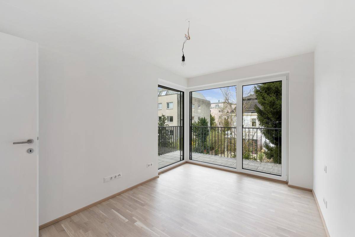 Helles Schlafzimmer mit Parkettboden und Zugang zu einem Balkon mit Blick ins Grüne.
