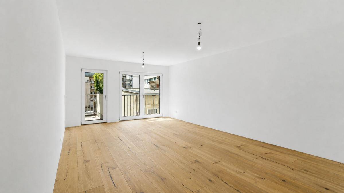 Heller, leerer Raum mit Holzboden und Zugang zu französischen Balkonen, ideal für Erstbezug.