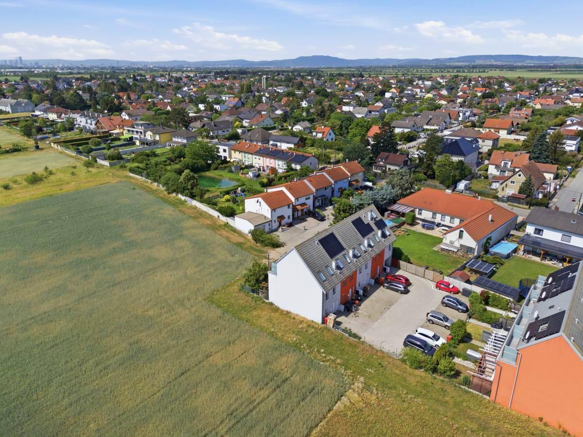 Weitläufige Luftaufnahme der Reihenhäuser, eingebettet zwischen Feldern und einer Wohnsiedlung.