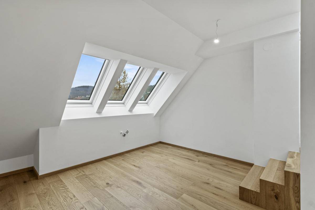 Helles Dachgeschosszimmer mit Holzboden, Dachfenstern und offenem Treppenaufgang.