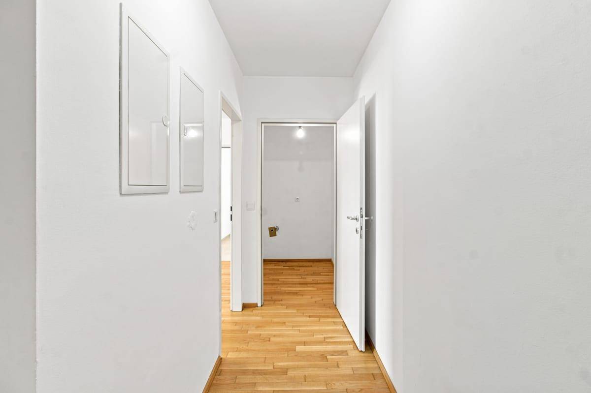 Heller Flur mit Holzboden und weißen Wänden, der zu weiteren Räumen führt.