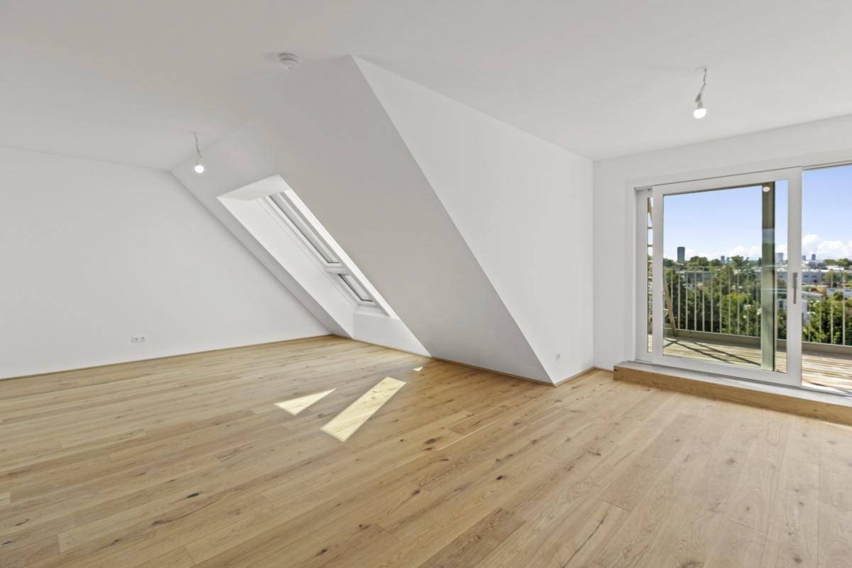 Heller Wohnraum im Dachgeschoss mit Holzboden, schräger Wand und Zugang zur Terrasse.