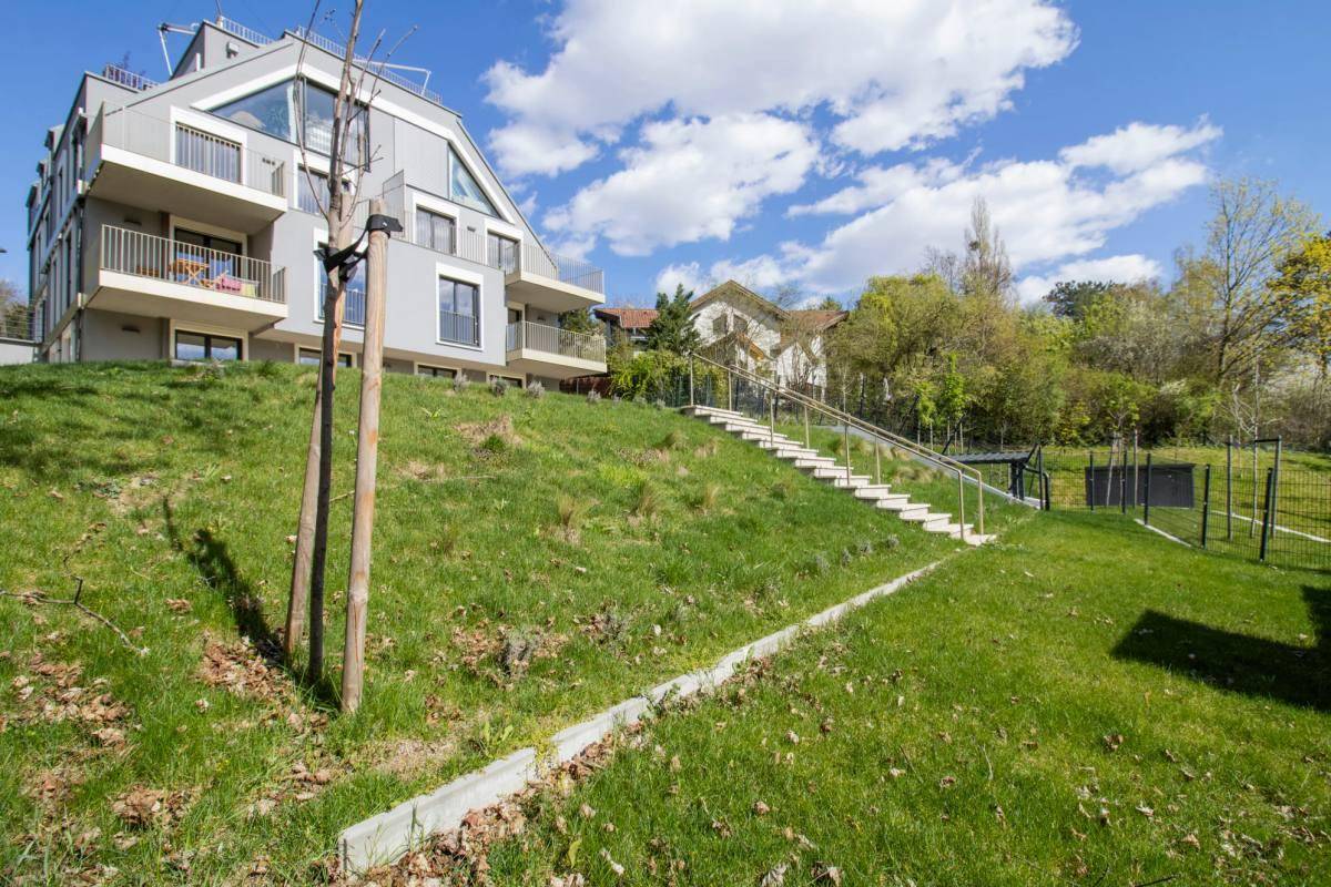 Seitenansicht des modernen Apartmentgebäudes, umgeben von einer grünen Landschaft mit Zugangstreppe.