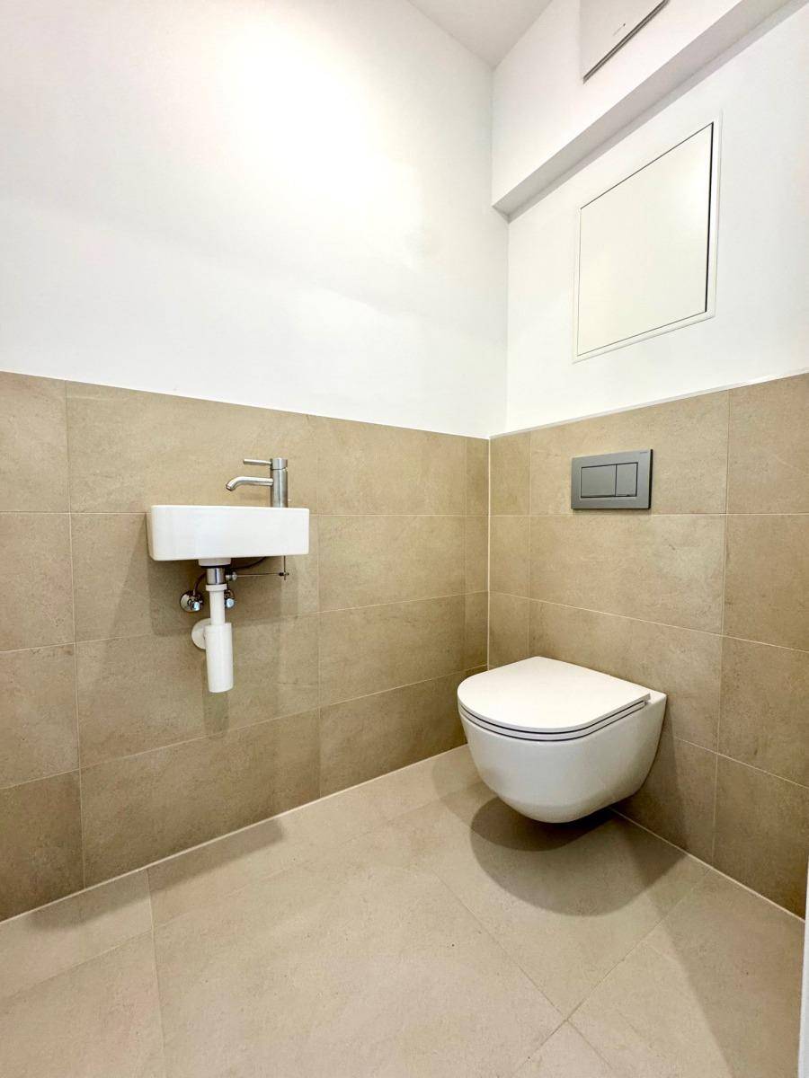 Modernes Gäste-WC mit Wand-WC, kleinem Waschbecken und beigefarbenen Fliesen.