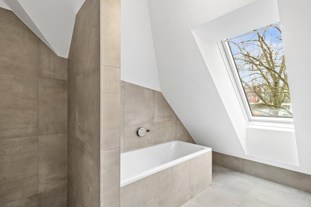 Modernes Badezimmer mit Badewanne, beigefarbenen Fliesen und einem Dachfenster für natürliches Licht.