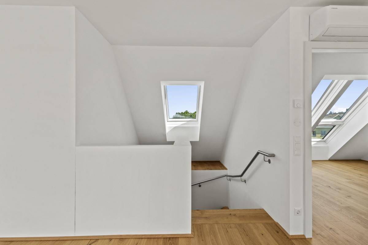 Heller Flurbereich im Dachgeschoss mit Holztreppe, Dachfenster und Handlauf.