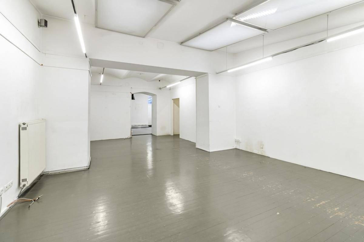 Heller, leerer Gewerberaum mit grau gestrichenem Holzboden und Heizkörper an der Wand, vielseitig nutzbar.