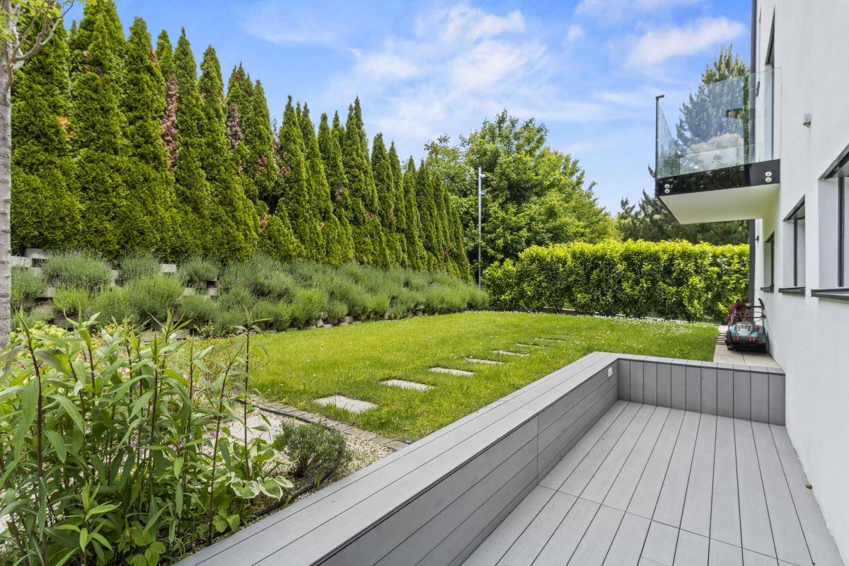 Grüner Garten mit Rasen, hohen Bäumen und einer kleinen Holzterrasse.