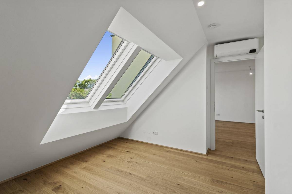 Helles Schlafzimmer mit Holzboden, Dachfenster und schräger Decke.