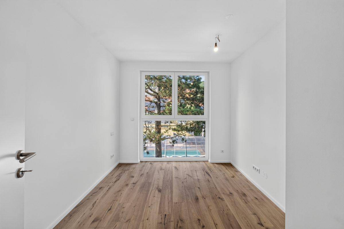 Helles Schlafzimmer mit großem Fenster und Holzboden, bietet einen Blick ins Grüne.