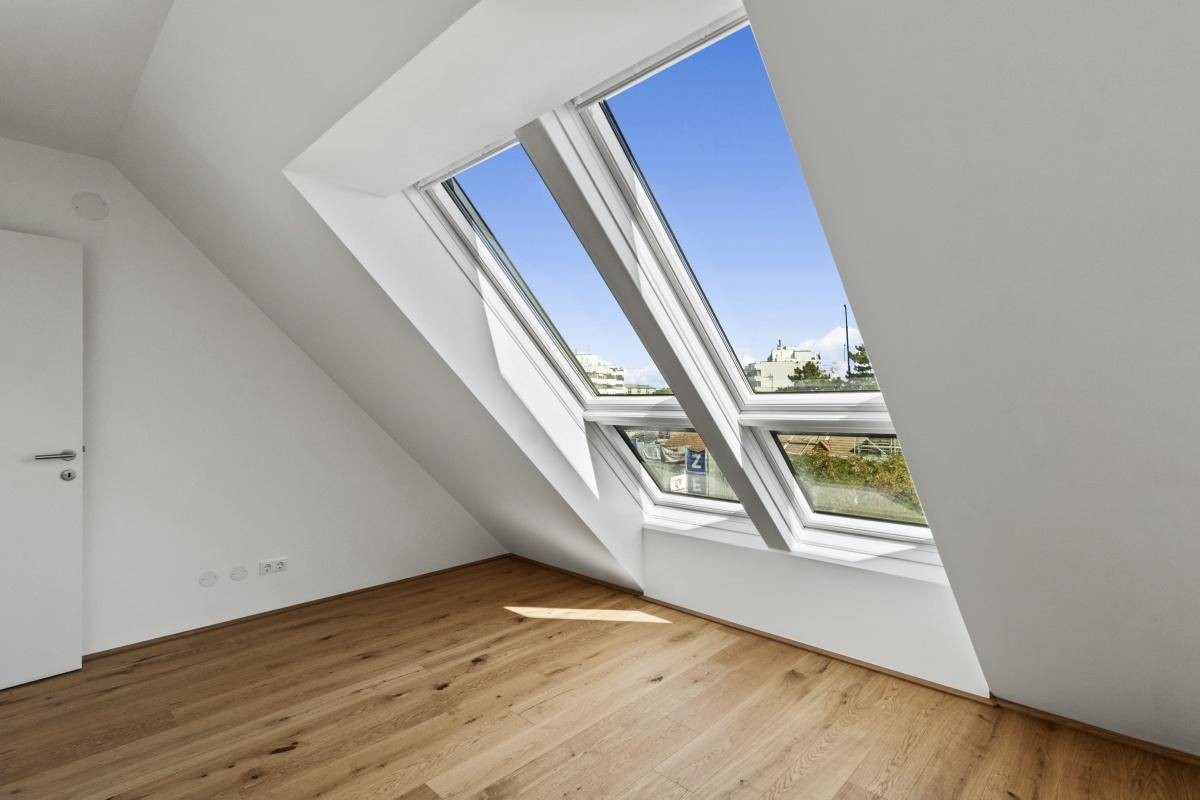Heller Raum im Dachgeschoss mit Holzboden, Dachschräge und mehreren großen Dachfenstern.