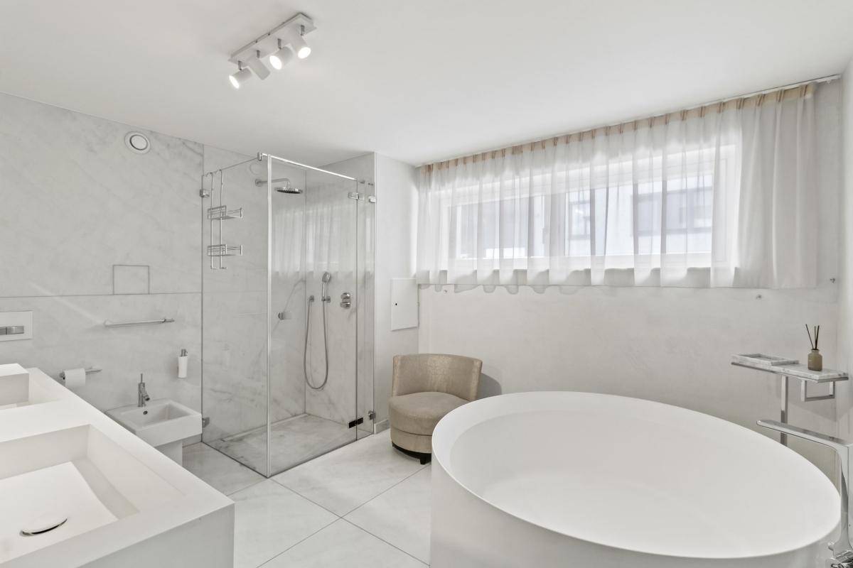 Luxuriöses weißes Badezimmer mit freistehender Badewanne, begehbarer Dusche und großen Fliesen.