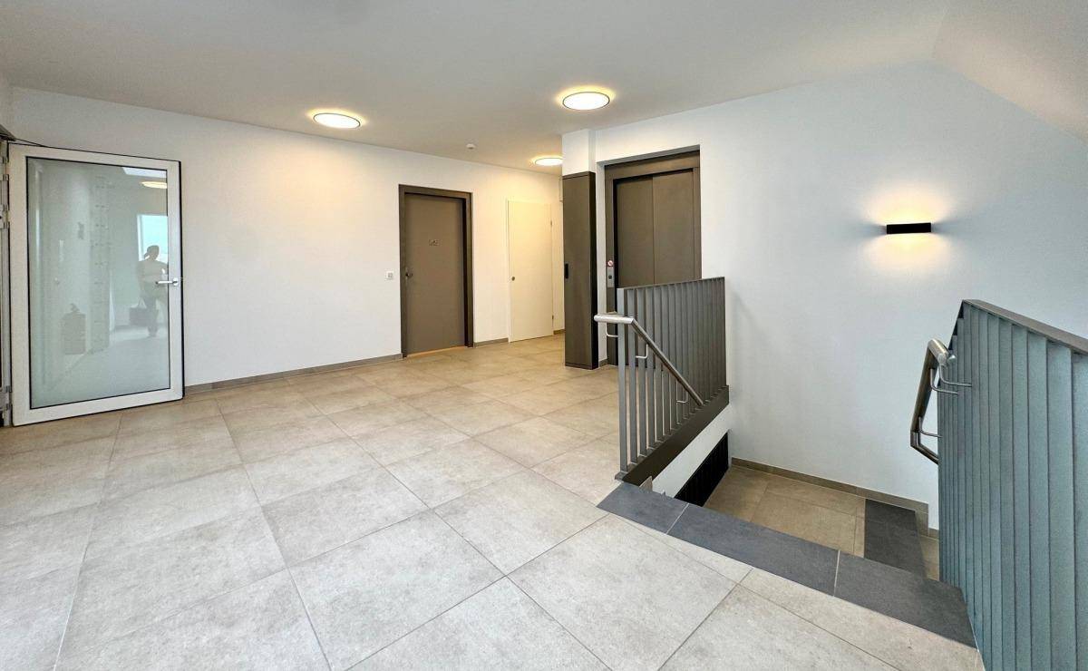 Heller Eingangsbereich mit Treppenhaus und Aufzug, der alle Etagen des Gebäudes verbindet.