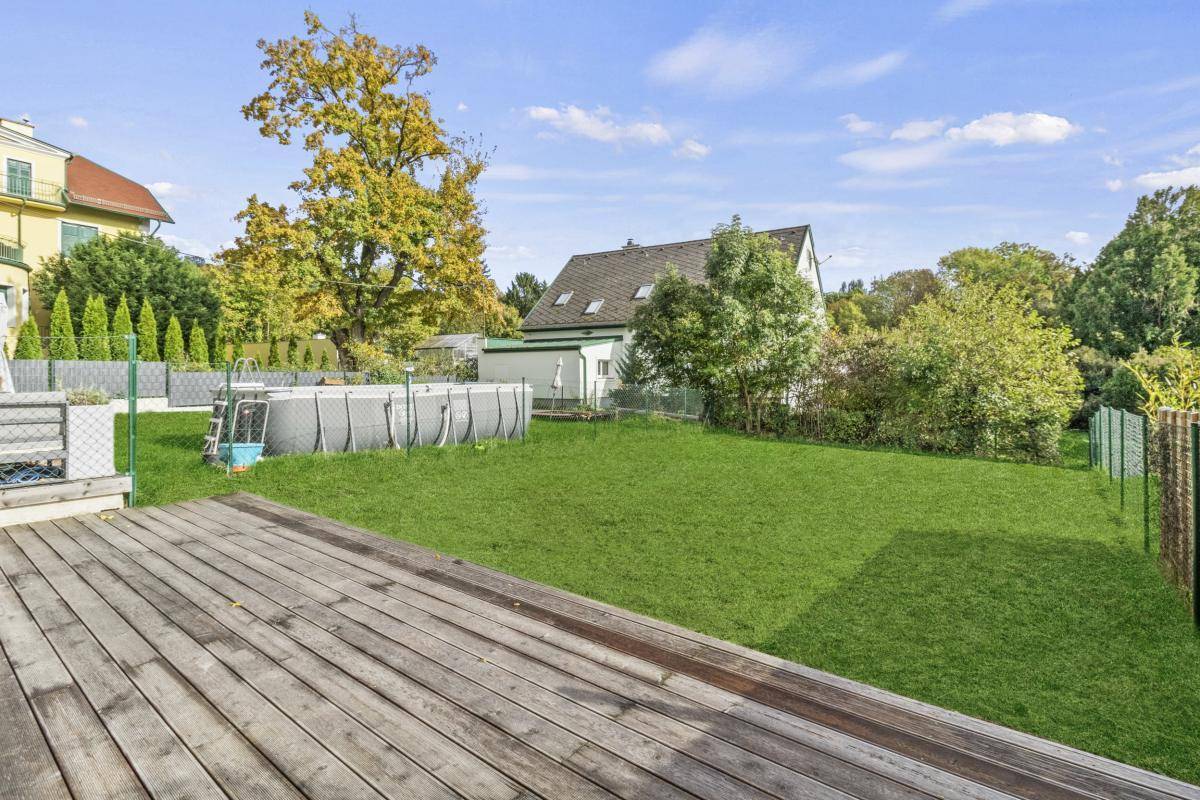 Großer Garten mit Rasenfläche, Holzterrasse und einem Aufstellpool.