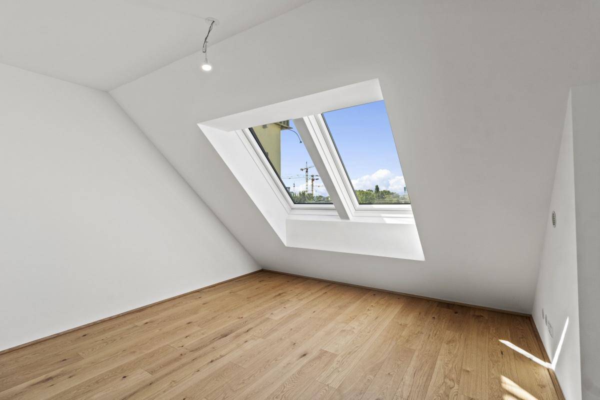 Helles Zimmer mit Holzboden und einem Dachfenster, ideal als Schlaf- oder Arbeitszimmer.