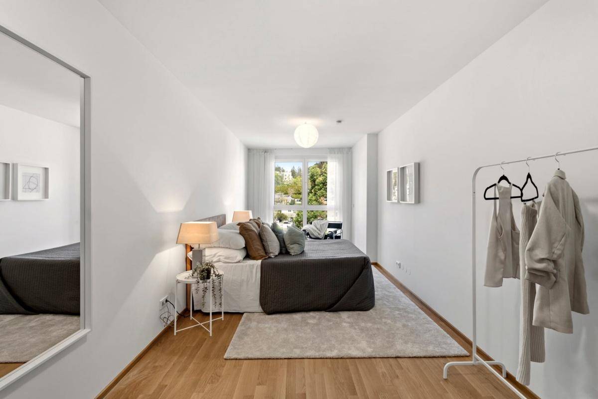Helles Schlafzimmer mit Parkettboden, großem Fenster und moderner Einrichtung.