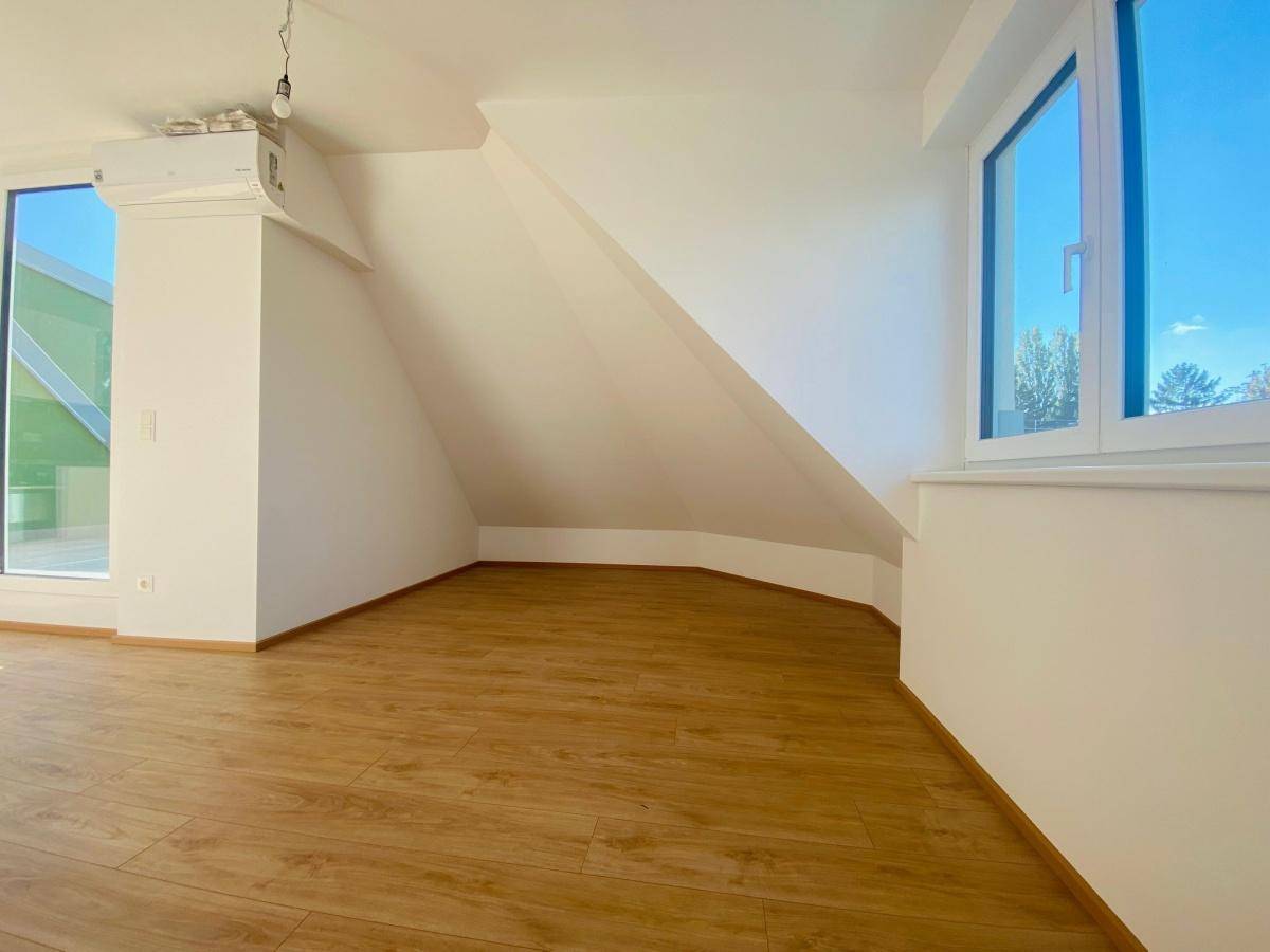 Heller Wohnraum mit Laminatboden, Dachschrägen und großen Fenstern für viel Tageslicht.