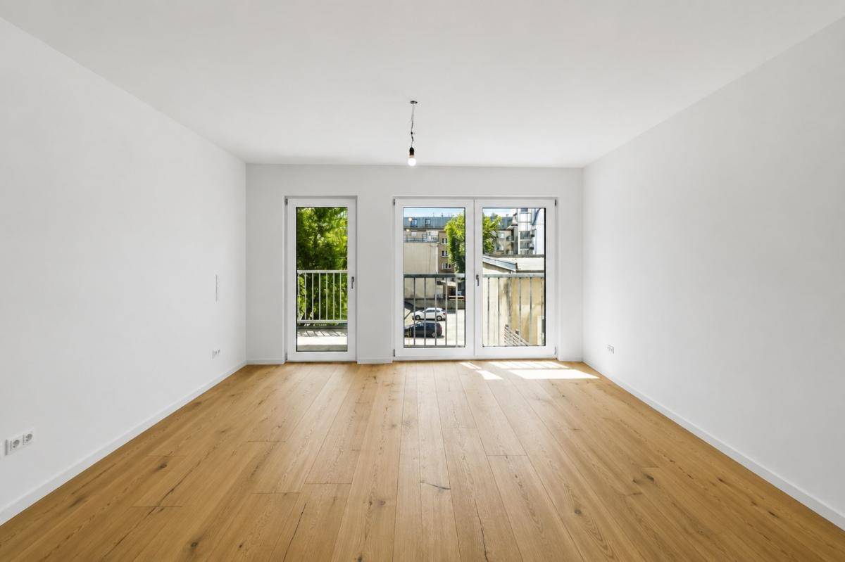 Lichtdurchfluteter Raum mit Holzboden und großen Fenstern, die den Blick ins Grüne freigeben.