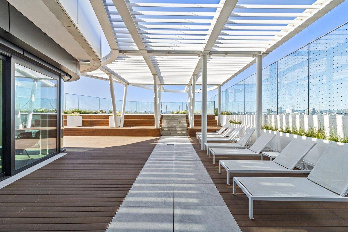 Weitläufige Dachterrasse mit Sonnenliegen, Pergola und beeindruckendem Stadtpanorama.