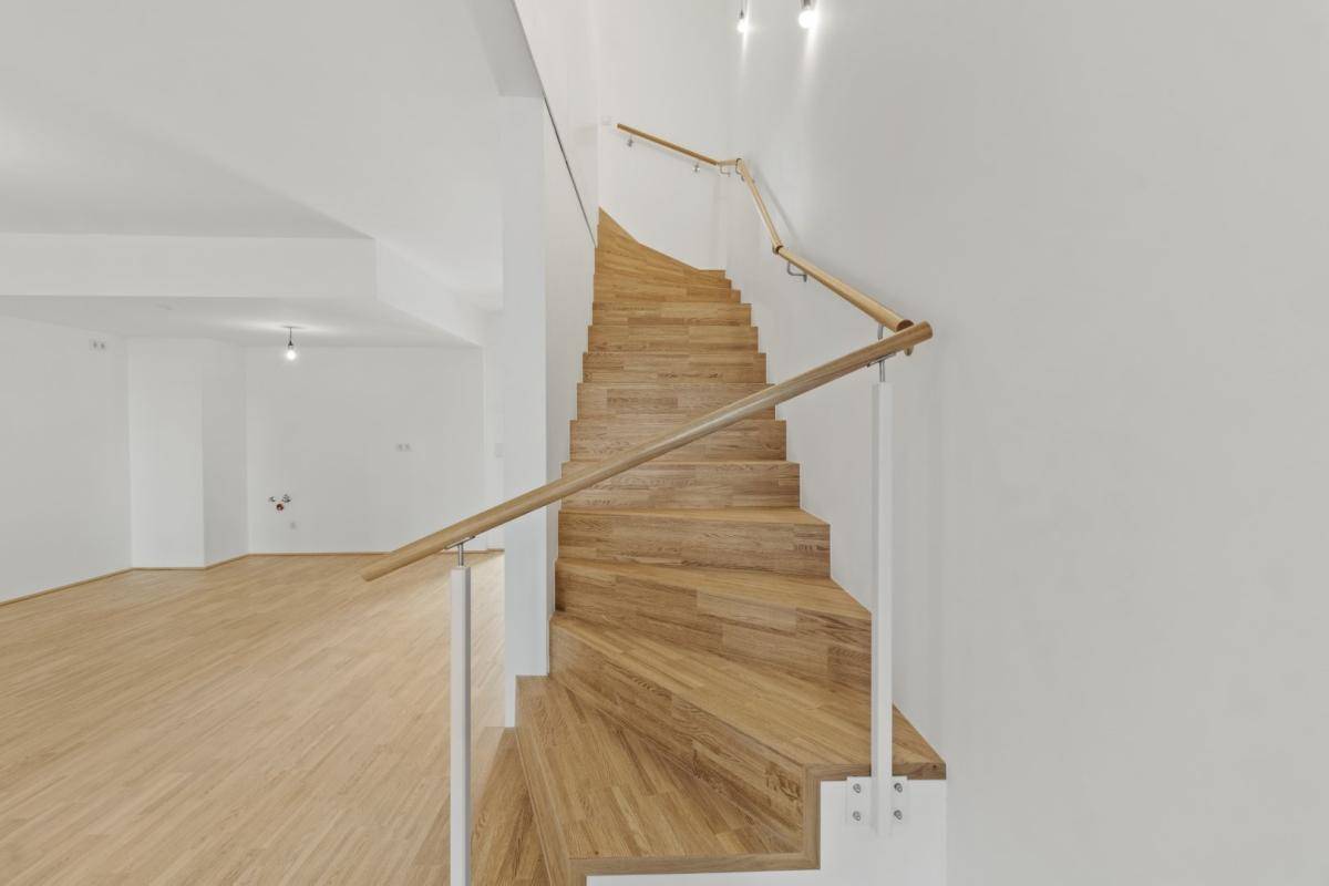 Moderne Holztreppe mit hellem Geländer, die die verschiedenen Ebenen der Wohnung verbindet.
