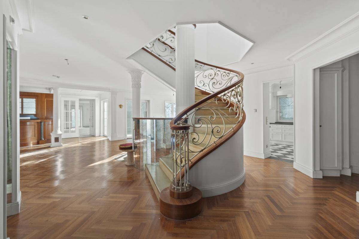 Elegantes Foyer mit geschwungener Holztreppe, schmiedeeisernem Geländer und Fischgrätparkettboden.