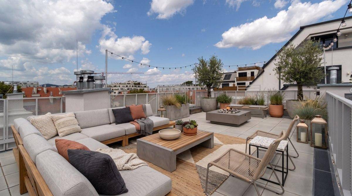 Große Dachterrasse mit moderner Lounge-Gruppe, Feuerstelle und Blick auf die umliegenden Gebäude.