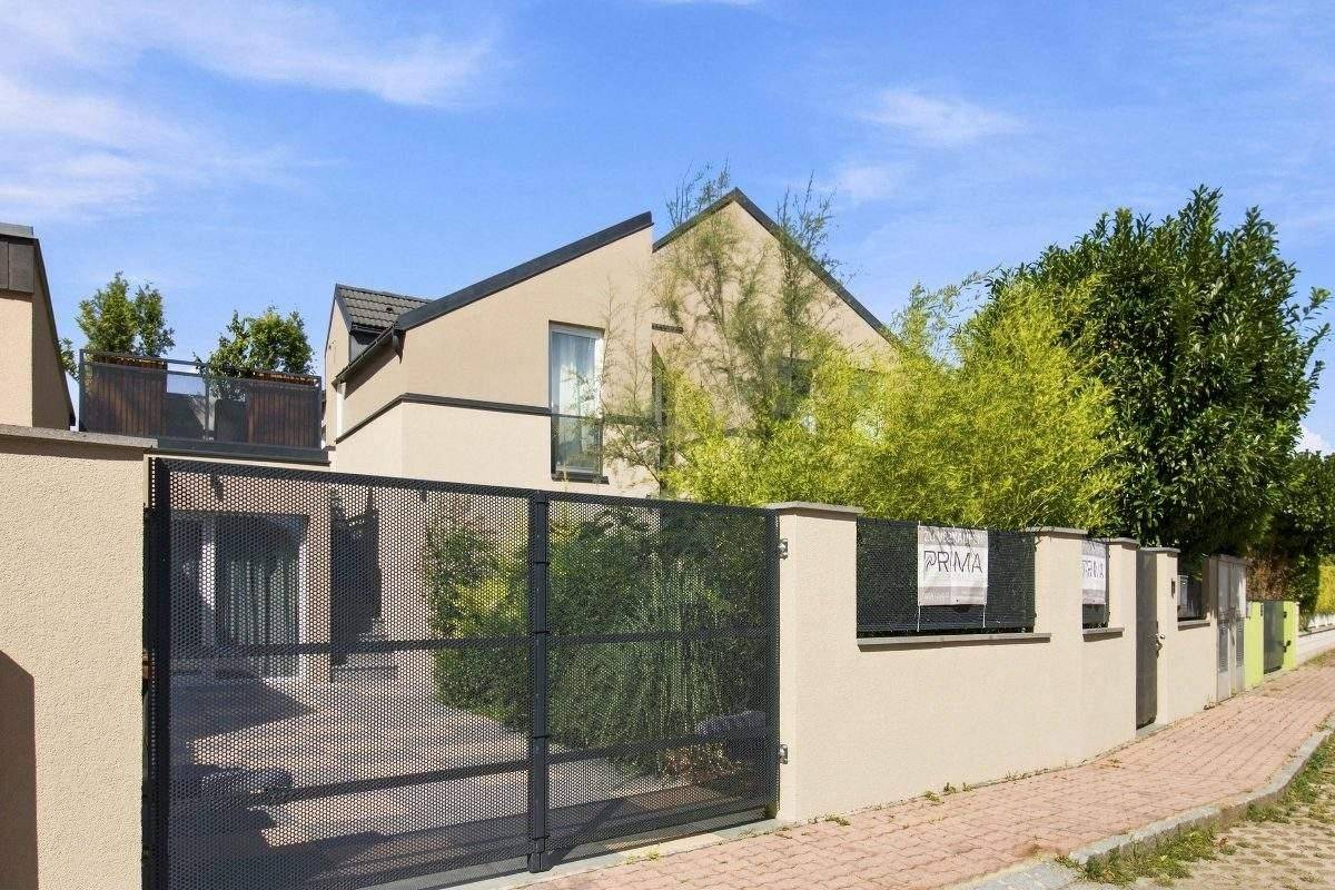Moderne Hausfassade mit Eingangstor und Zaun, umgeben von üppigem Grün.