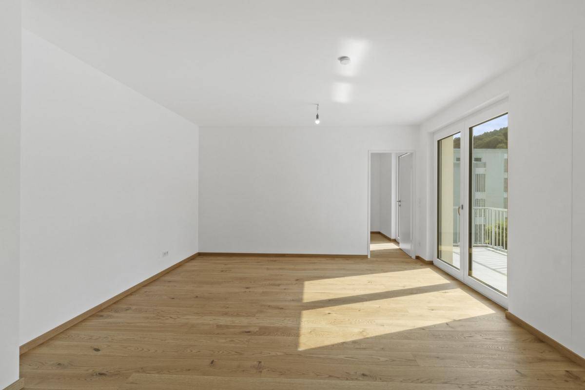 Geräumiges Wohnzimmer mit hellem Holzparkettboden und Zugang zu einem Balkon.