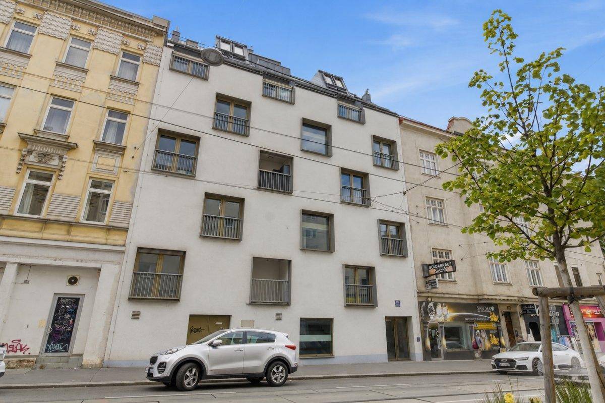 Moderne Gebäudefassade mit zahlreichen Fenstern und kleinen Balkonen an einer belebten Straße.