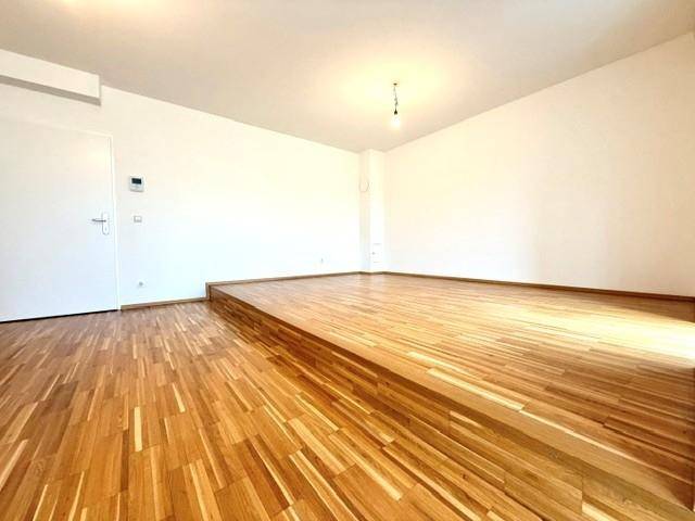 Leerer Raum mit glänzendem Parkettboden und weiß gestrichenen Wänden, bereit zur Einrichtung.